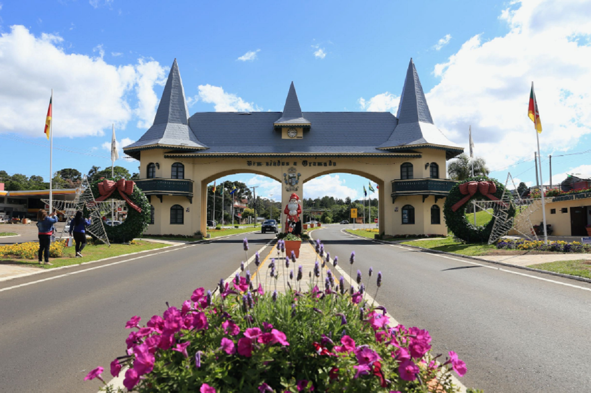 Fachada da entrada principal de Gramado, com pórtico em estilo alpino e letreiro de boas-vindas cercado por jardins